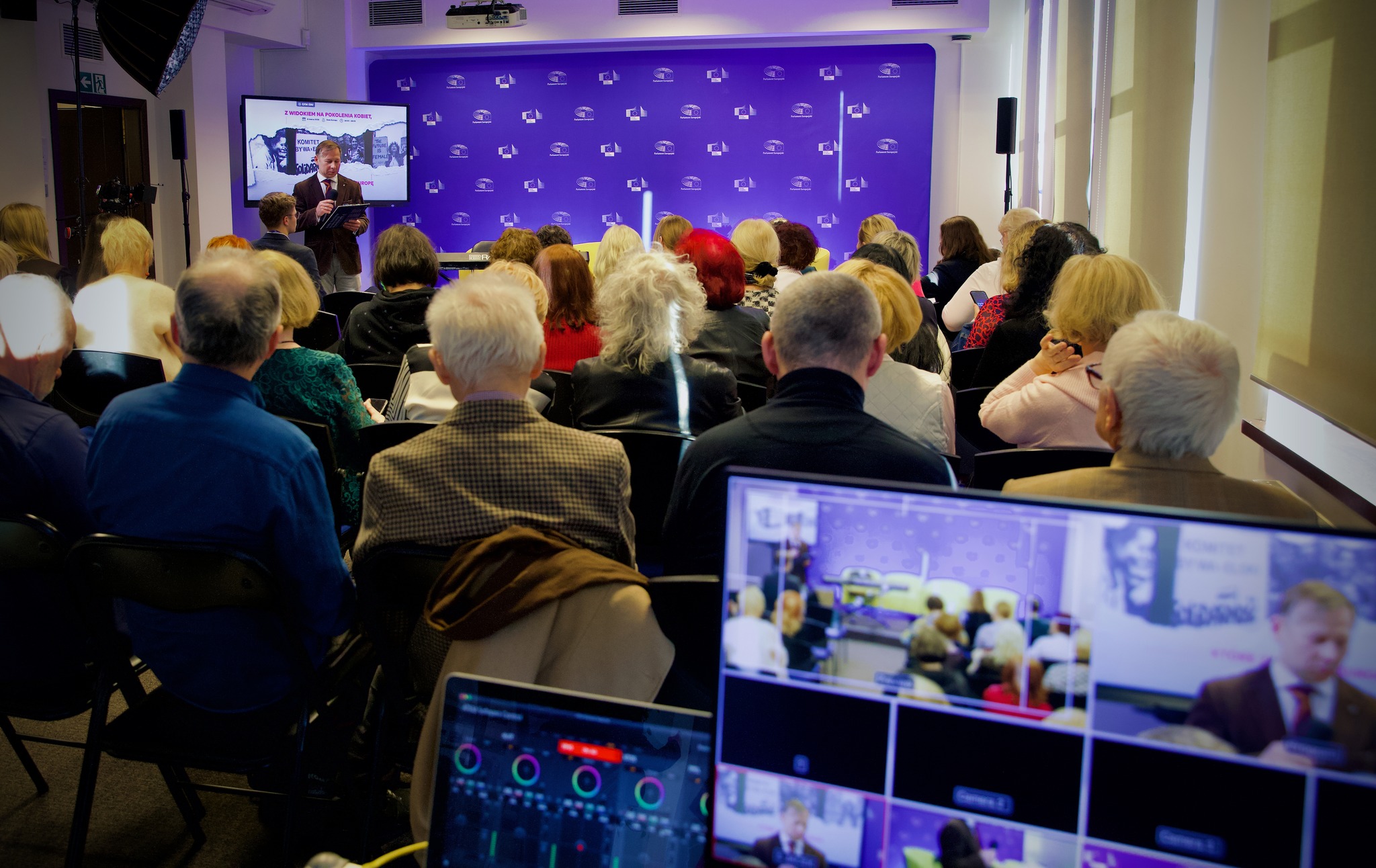 Szeroki kadr na którym widoczna jest scena na której siedzą uczestniczki debaty. Przed nimi widoczna jest widownia. 
