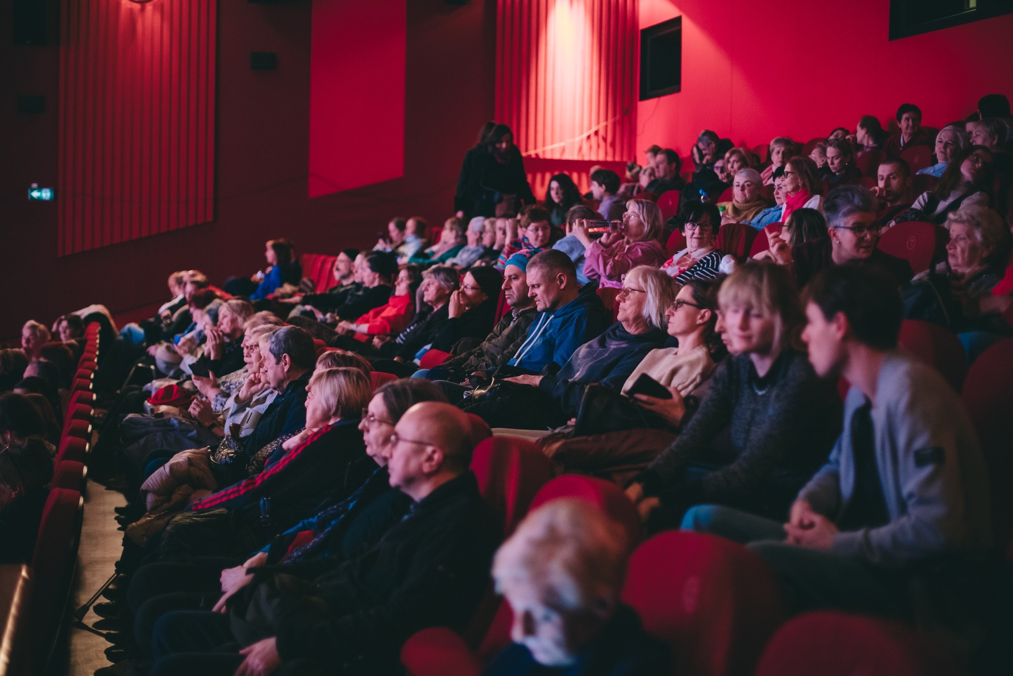 szerokie ujęcie przedstawiające tłum osób siedzący w kinie, oglądający film. 
